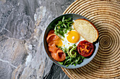 Healthy breakfast bowl with fried eggs, salmon, avocado, grilled tomato and salad