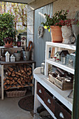 Firewood, gardening utensils and vintage-style decorations on shelves against outside wall