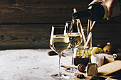 Weißwein neben Käseplatte in Glas einschenken