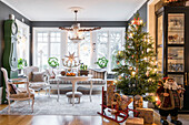 Round table, crystal chandelier above, seating, grandfather clock and illuminated Christmas tree in salon