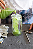 Woman pours matcha tea into a glass with ice cubes