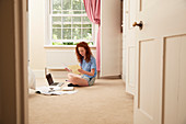 Preteen girl doing homework at laptop on bedroom floor