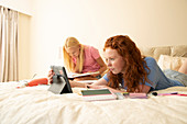 Friends with digital tablet doing homework on bed