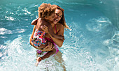 Happy mother holding daughter in summer swimming pool