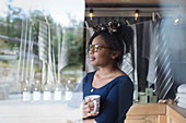 Thoughtful female shop owner drinking coffee at window