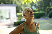 Happy senior woman with headphones exercising in garden