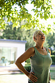 Happy senior woman with headphones exercising in garden