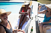 Senior women friends drinking champagne at summer poolside