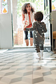 Happy baby daughter running to greet mother at doorway
