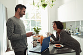 Happy couple enjoying breakfast and working at laptop