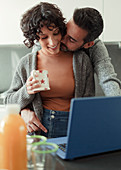 Husband kissing wife working from home at laptop