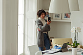 Woman with smart phone working from home at window