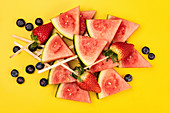 Wassermelonenschnitze und Beeren auf gelbem Hintergrund