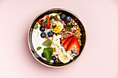 Oat granola with fresh berries, banana, yogurt, maple syrup, seeds and mint leaves