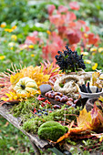 Table with moss, autumn leaves, chestnuts, berries, ornamental pumpkin, straw wreaths, and wreath tying tools