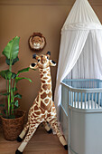 Indoor plant and giraffe figurine next to baby bed with canopy