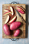 Whole and sliced red potatoes on a wooden cutting board