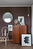 Cupboard, modern artworks, chair and mirror in corner of room with dark wall