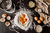 Egg yolks in flour on with utensils and ingredients for cake