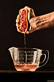 Hand squeezing grapefruit juice in glass jug