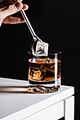 Pouring ice cube into Old fashioned cocktail