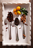 Star anise, cloves, cinnamon sticks on spoons next to kumquats