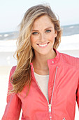 A young woman on the beach wearing a pale top and a salmon-pink leather jacket