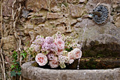 Fragrant spring bouquet of lilacs and roses in basin of wall fountain