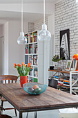 Fruit basket and tulips on dining table with wooden top below industrial lights