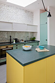 Kitchen island with yellow front in open kitchen with white painted brick wall