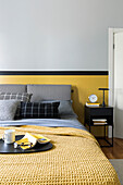 Doppelbett mit grauem Bettkopfteil und gelber Tagesdecke