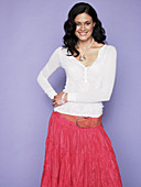 A dark-haired woman wearing a white shirt and a pink skirt