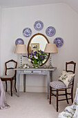 Antique, decorative wall plates and oval mirror above old wooden table