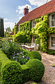 Table and chairs with clipped hedges in garden of charming family home.