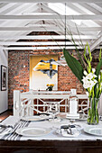 View across set table to brick wall below open roof structure