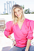 Junge blonde Frau in pink Wickelbluse mit Puffärmel und Jeans