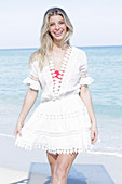 A young blonde woman wearing a white embroidered summer dress