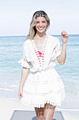 A young blonde woman wearing a white embroidered summer dress