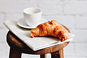 Frühstückscroissant, Tasse Kaffee und Zeitung auf Holzhocker