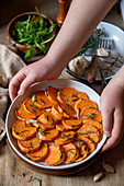 Hands holding a baking form with roasted sweet potatoes
