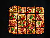 Bunte Pizza vom Blech mit Salami in Stücke geschnitten