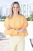 Junge blonde Frau in apricotfarbener Bluse und heller Hose