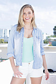 A young blonde woman wearing a mint top, a denim shirt and shorts