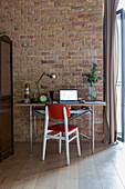 Schreibtisch mit rotem Stuhl vor Ziegelwand