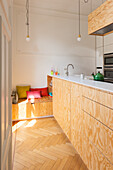 Küchentheke mit heller Sperrholzfront und integrierte Sitzbank mit bunten Kissen