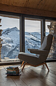 Armchair and stack of books next to window with view of mountain landscape