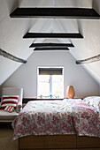 Simply furnished attic bedroom with French 19th century linen-covered armchair next to the bed