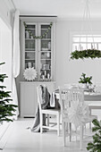 Table and chairs below suspended Christmas wreath and glass-fronted cabinet in bright dining room