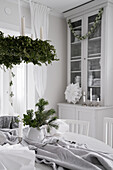Festively set dining table below suspended Christmas wreath and glass-fronted cabinet in bright dining room