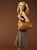 A blonde woman wearing a brown top and a skirt with a shopping bag